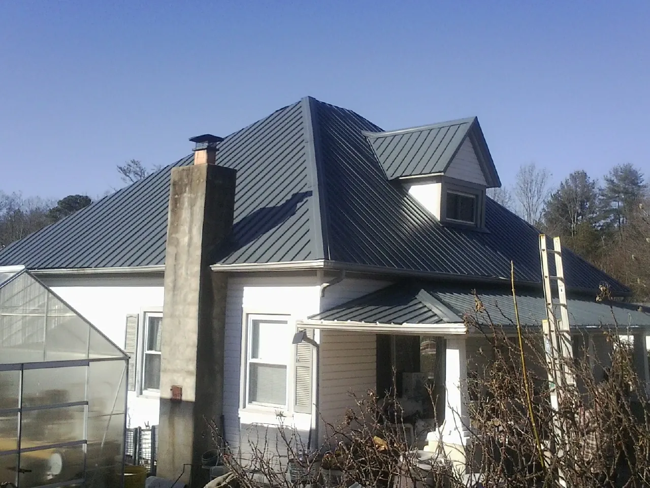 Dark blue standing seam metal roof on a white farmhouse with dormer — Slate & Tile Roof Repair by Roofing Brothers in Buffalo Lake
