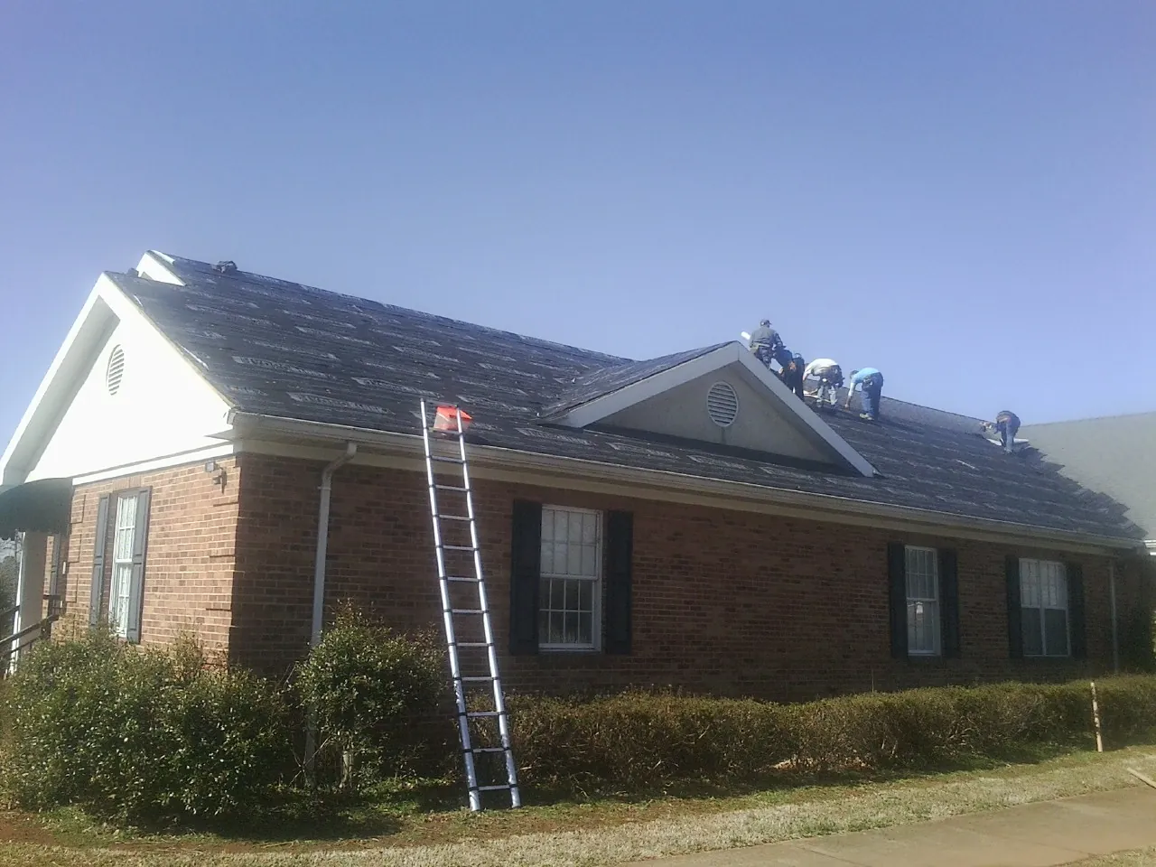 Crew tearing shingles off a brick ranch roof with a ladder set — Emergency Roof Repair work by our crew in Buffalo Lake