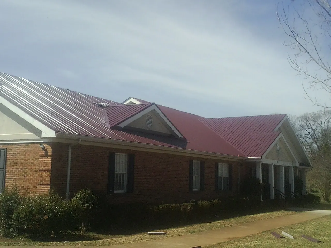 Red metal roof with gabled entries on a long brick building, from a Hail Damage Roof Repair job in Buffalo Lake