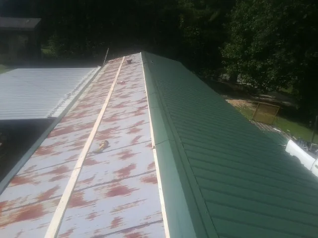 Old rusted panels beside newly installed green metal roofing — Wind Damage Roof Repair by Roofing Brothers in Buffalo Lake