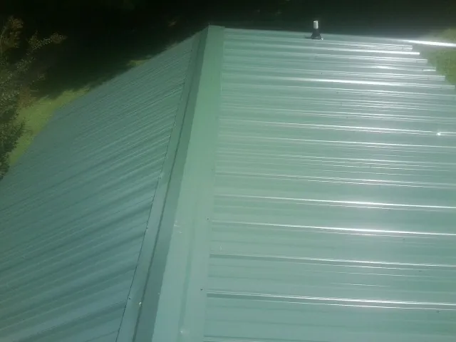 New green metal panels meeting at the ridge of a roof — Flat Roof Repair work by our crew in Buffalo Lake