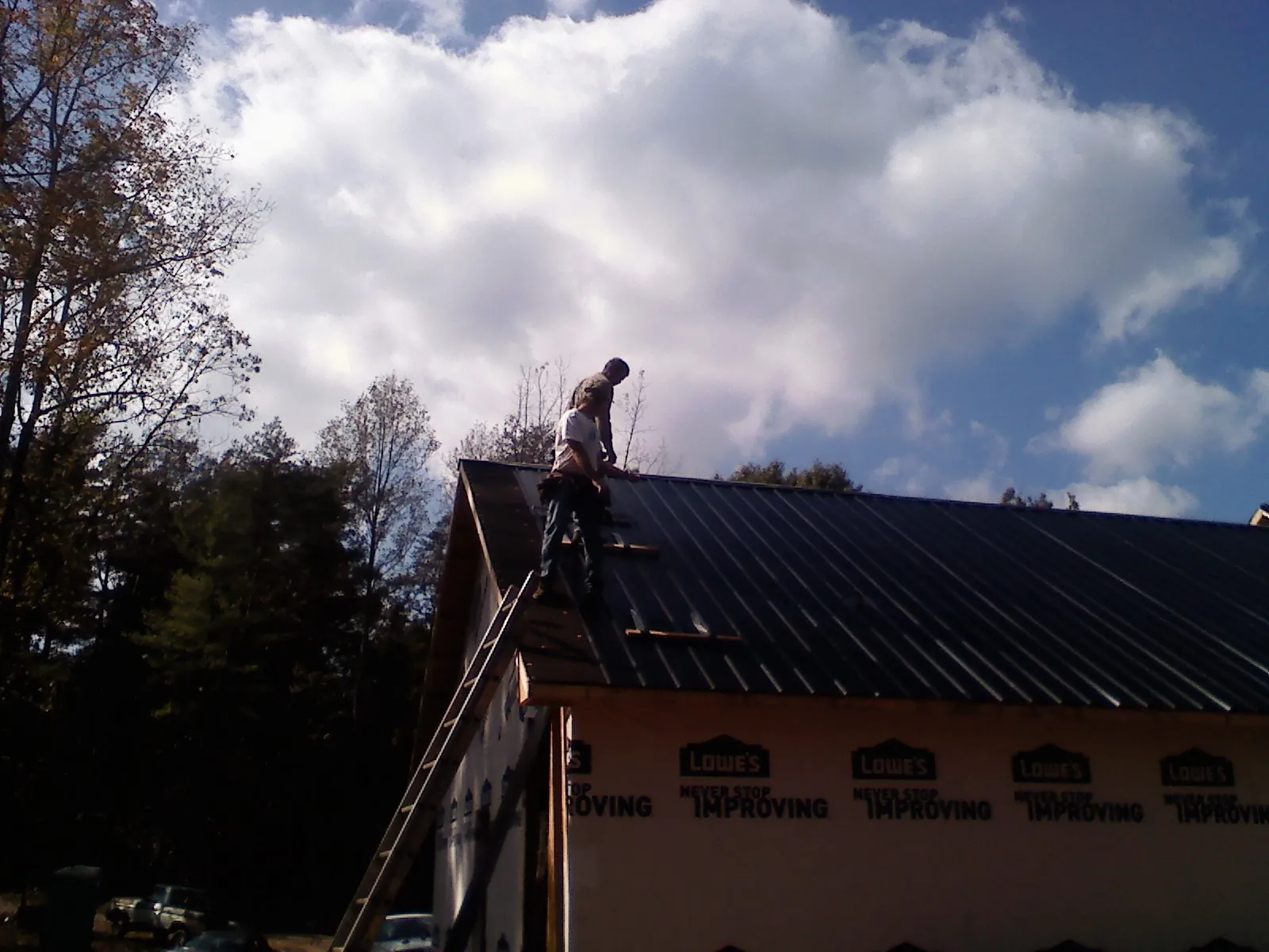Roofer fastening dark metal panels high against a cloudy sky, from a Roof Inspection job in Buffalo Lake