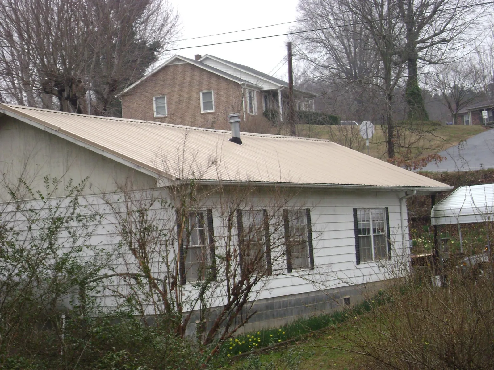 Tan metal roof on a white sided house set into a hillside — Commercial Roofing by Roofing Brothers in Buffalo Lake
