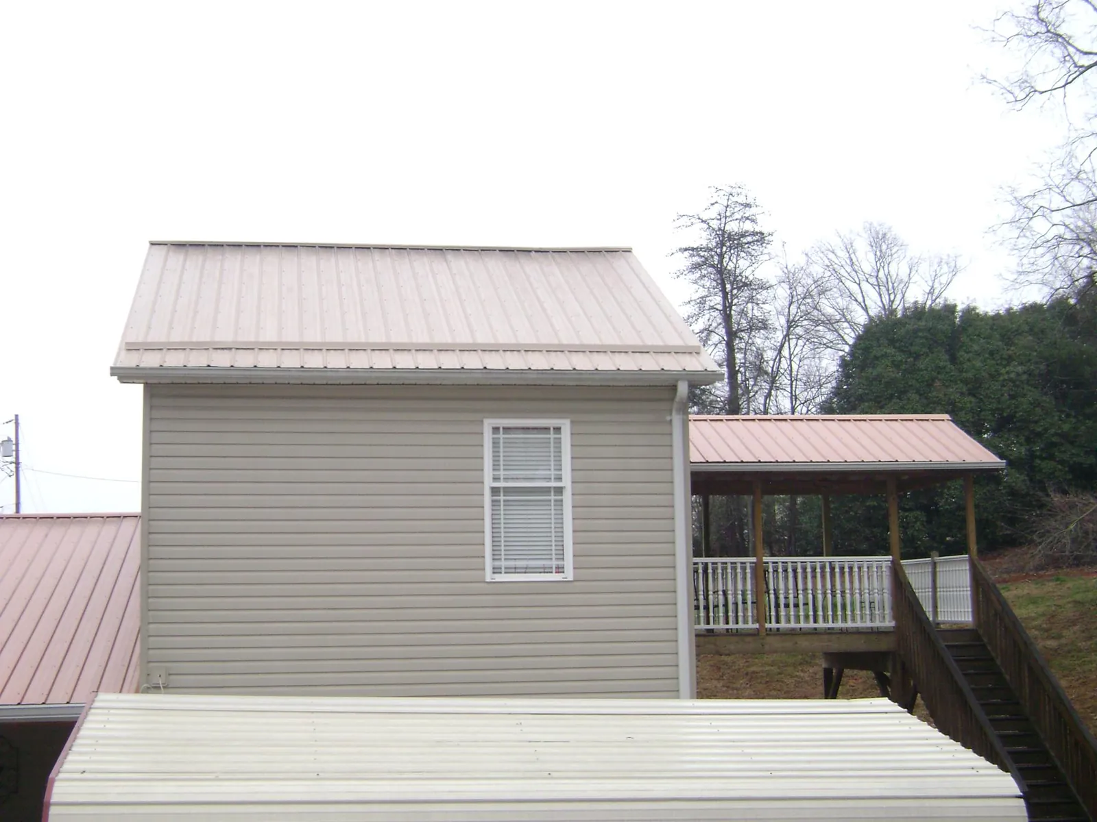 Tan metal roofs on a two story addition and attached porch, from a Roof Replacement job in Buffalo Lake